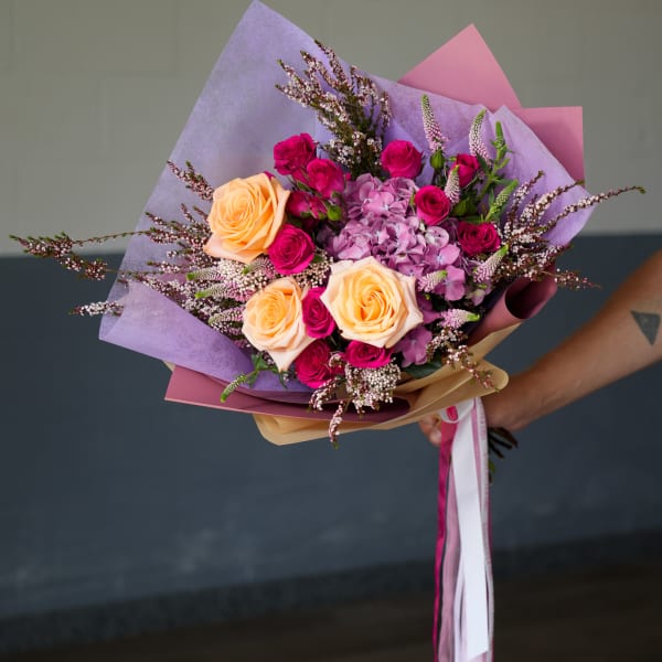 Handheld bouquet of pink and peach roses with lavender flowers
