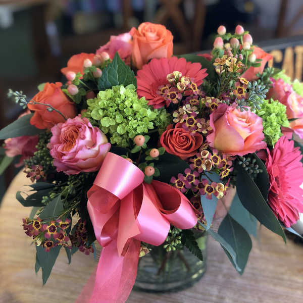 Pink and coral bouquet with roses, gerbera daisies, and a ribbon in a glass vase