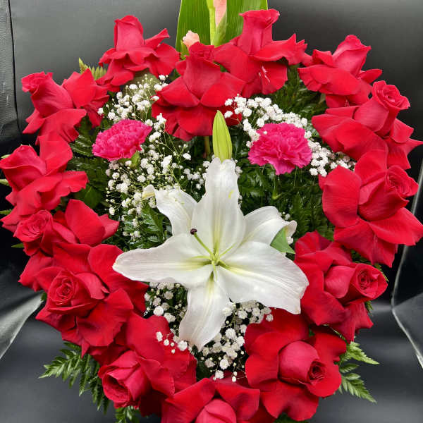 Heart-shaped arrangement of red roses with a central white lily and pink carnations