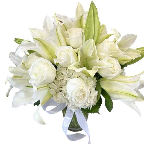 White roses and lilies arranged in a glass vase with a pale ribbon