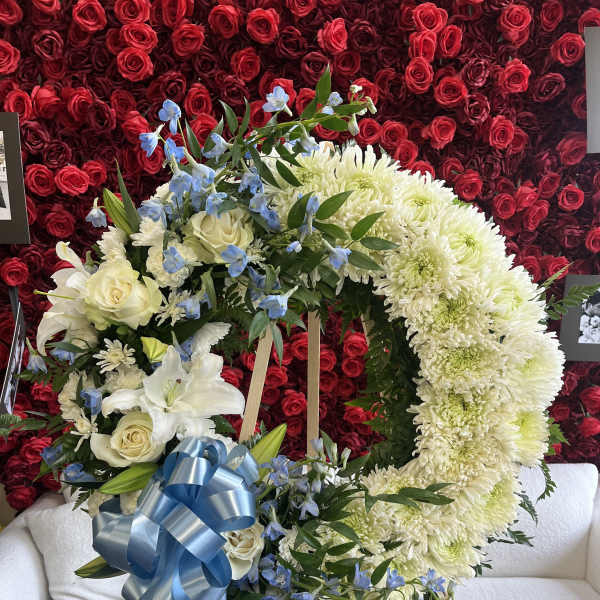 Heart-shaped floral wreath with white flowers, blue accents, and a blue ribbon