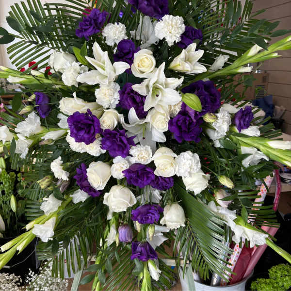 White lilies, roses, and purple blooms in a large standing spray