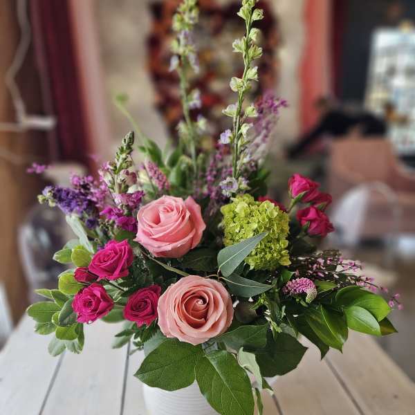 Pink and magenta roses in a white vase with mixed greenery