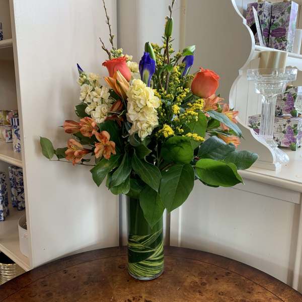 Mixed bouquet in a tall glass vase with orange, cream, and blue flowers