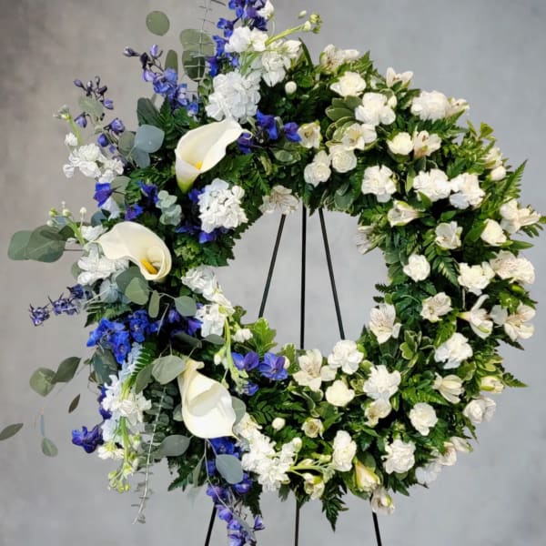 Large floral wreath with white calla lilies and blue flowers on a stand