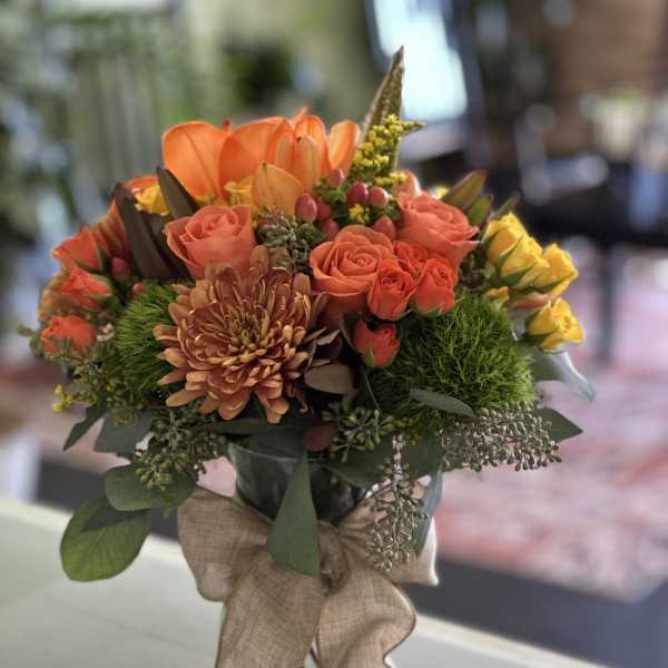 Orange and coral bouquet in a clear glass vase with a burlap ribbon