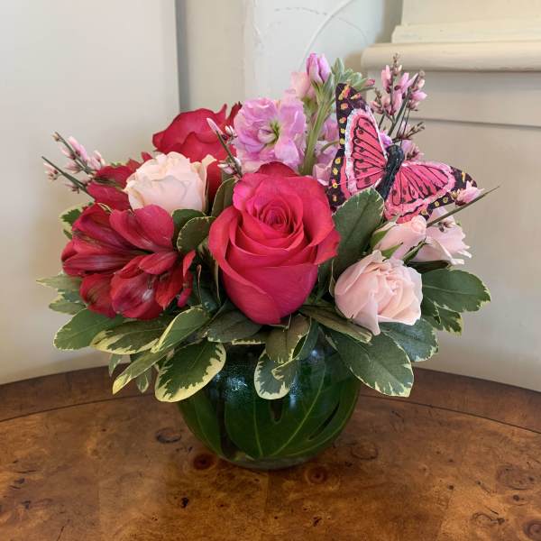 Pink and red rose arrangement in a green glass vase with a butterfly pick