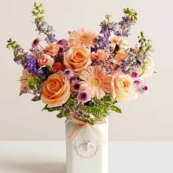 Peach roses and purple flowers in a white vase