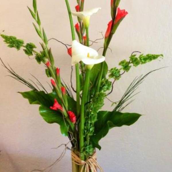 Tall floral arrangement with white calla lilies and red gladiolus in a glass vase