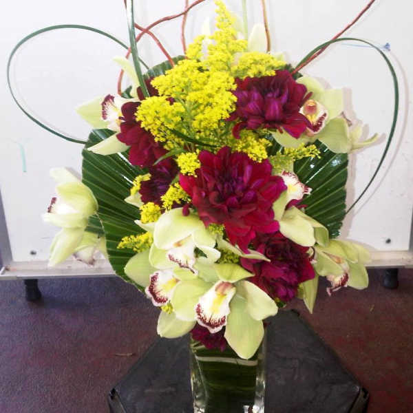 Bouquet of burgundy and pale green orchids with yellow filler in a glass vase