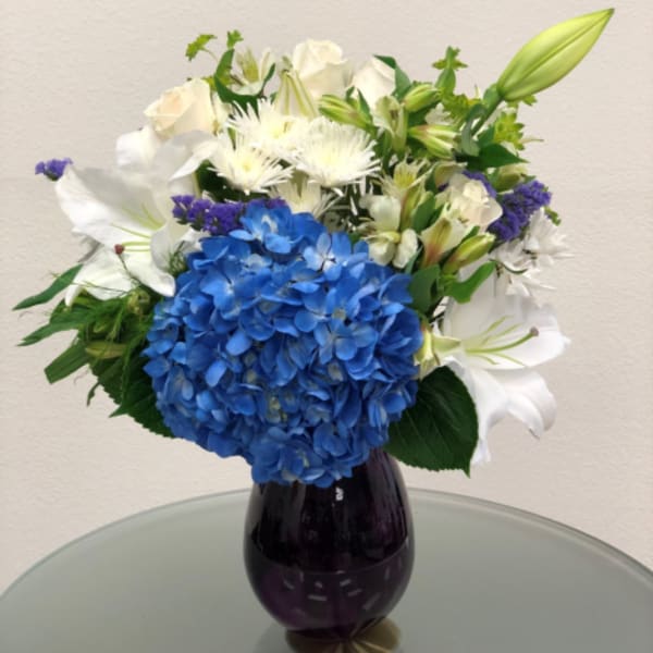 Blue hydrangea and white lily bouquet in a dark glass vase