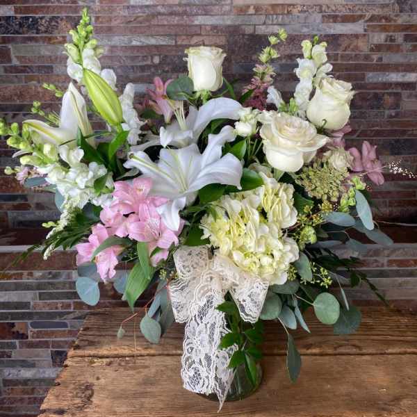 White lilies and roses with pink blooms in a glass vase with lace ribbon