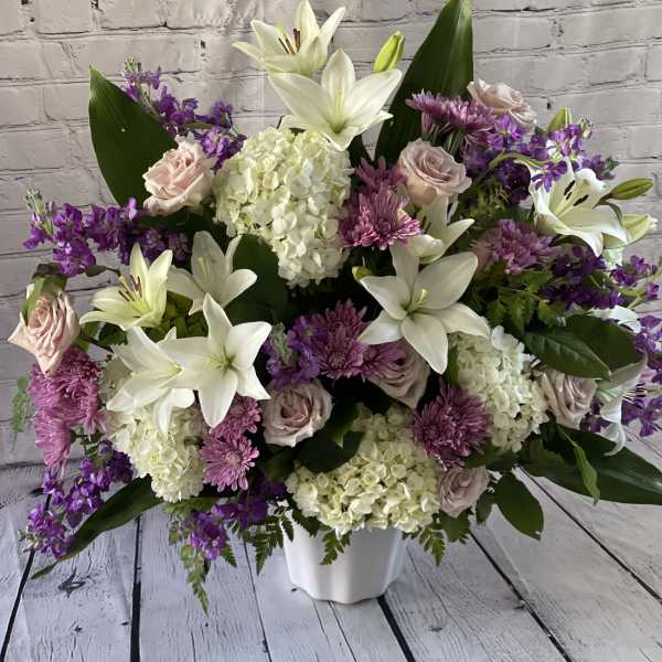 Large bouquet of white lilies, pink roses, and purple flowers in a white vase