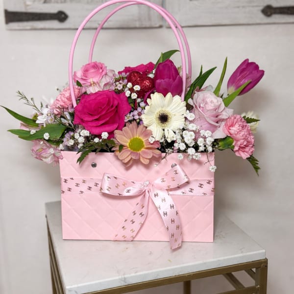 Pink handbag-style flower arrangement with pink roses, tulips, daisies, and accent blooms.