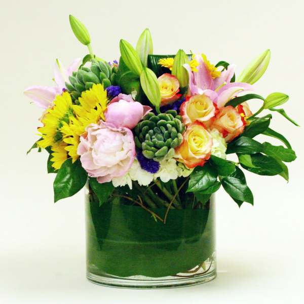 Mixed bouquet of pink lilies, yellow daisies, and roses in a glass vase