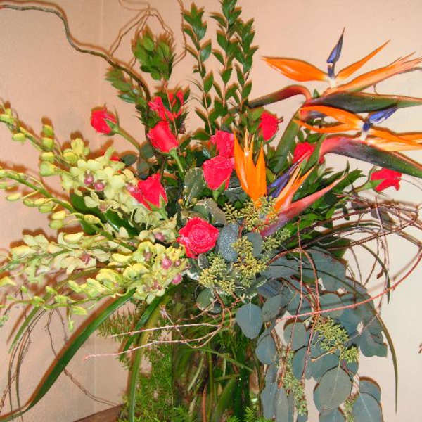 Tall tropical arrangement with orange bird-of-paradise and pink roses in a glass vase