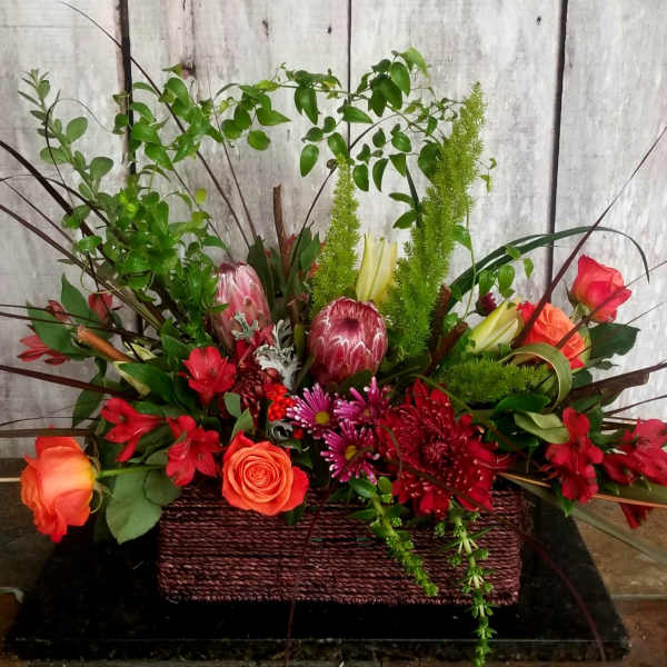 Mixed floral arrangement in a rectangular basket with red and orange blooms