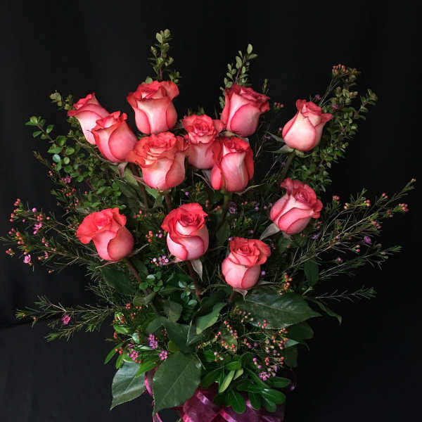 Pink roses arranged in a clear glass vase with a purple ribbon