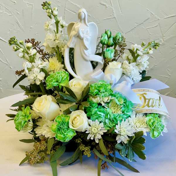 White floral arrangement with roses, carnations, and a ceramic angel figure