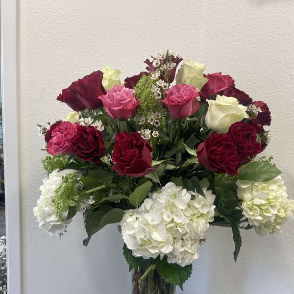 Tall glass vase with white hydrangeas and red, pink, and cream roses in a mixed arrangement