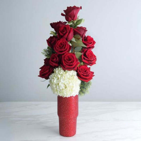 Tall red vase with a column of red roses above a white hydrangea cluster
