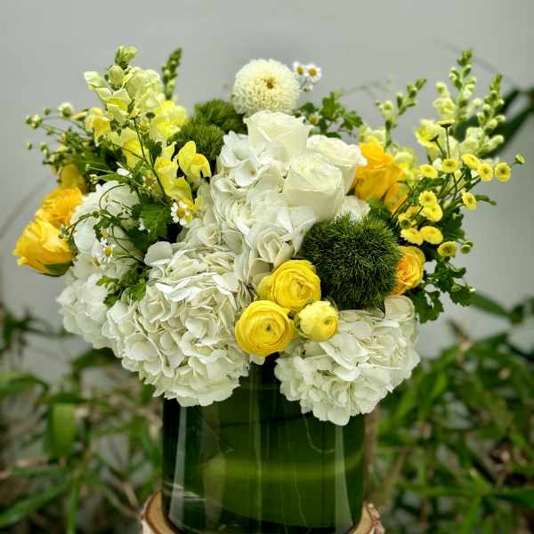 White and yellow flower arrangement in a green glass vase
