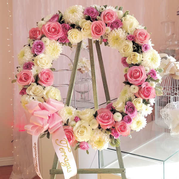 Heart-shaped floral wreath with pink, cream, and purple roses on a stand