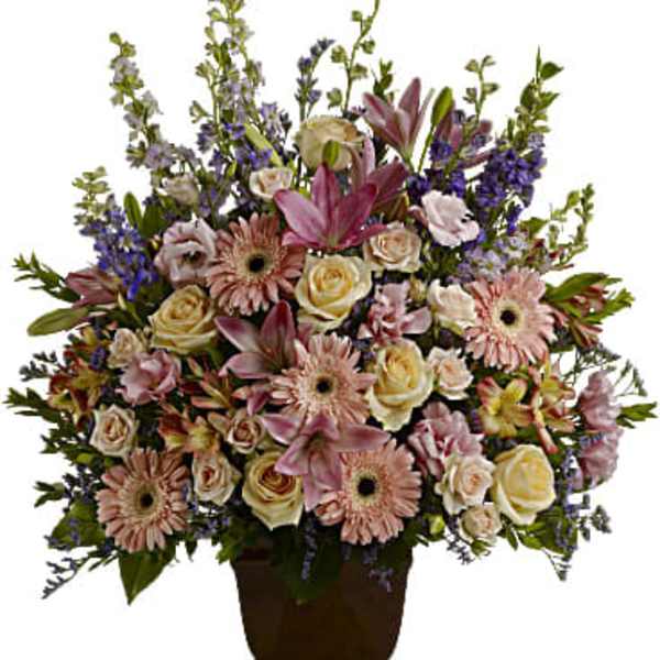 Tall arrangement of pink lilies, gerbera daisies, and cream roses in a brown urn-style vase