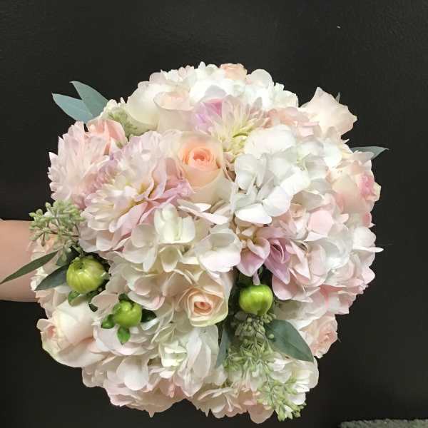 Handheld bouquet of pale pink and white flowers with green accents