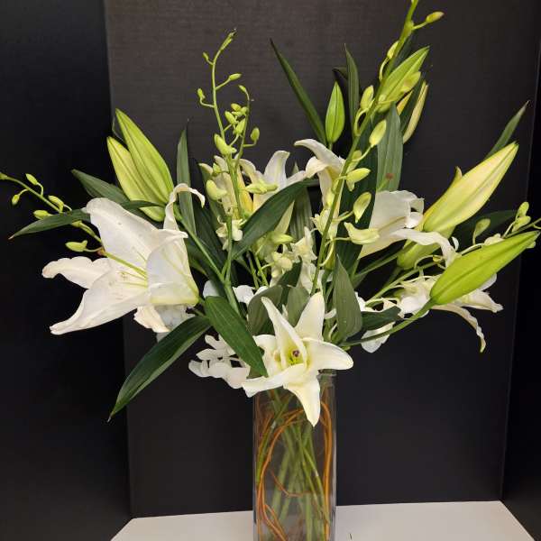 White lilies and orchid stems in a tall glass vase