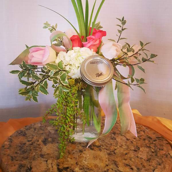 Pink and white floral arrangement in a glass jar with a ribbon and mason jar lid
