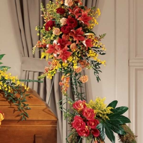 Tall funeral spray with red lilies, roses, and yellow filler flowers