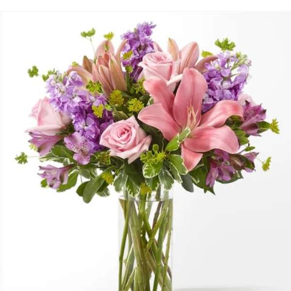 Pink lilies and roses in a clear glass vase with purple flowers