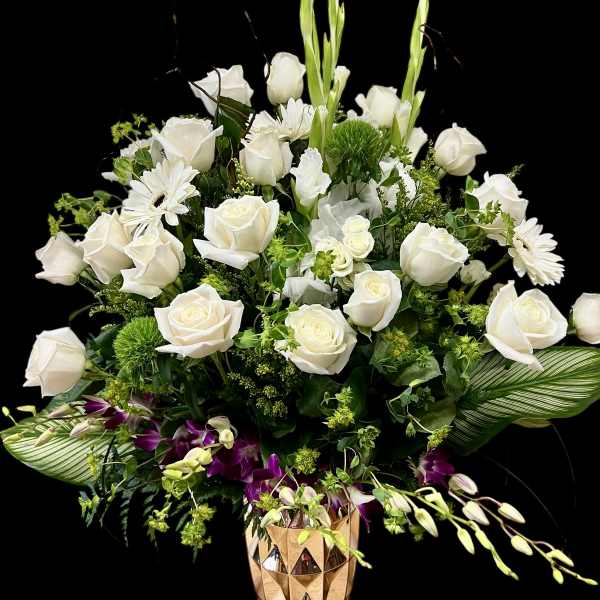 Tall white and green flower arrangement with purple orchids in a gold geometric vase