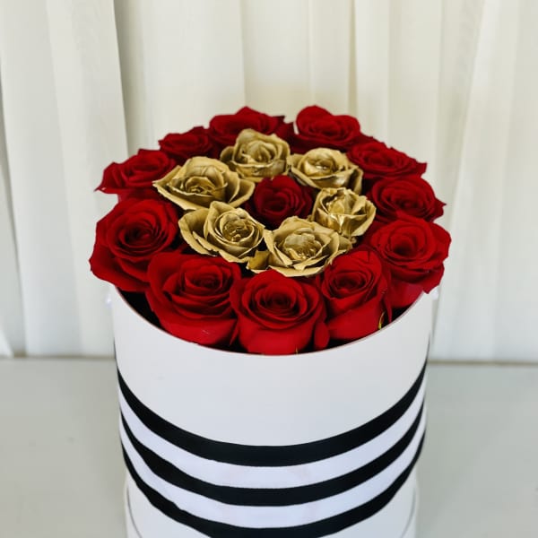 Red and gold roses arranged in a round white box with black stripes