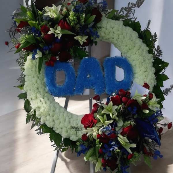 Floral funeral wreath with blue "DAD" lettering on a stand