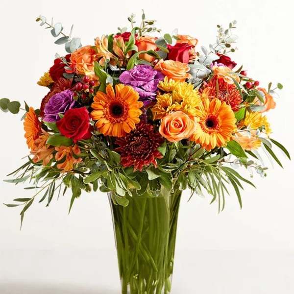 Mixed bouquet of orange, red, and purple flowers in a clear glass vase