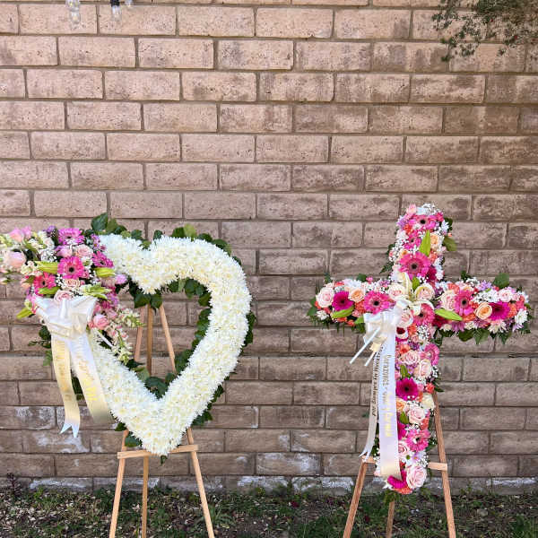 Two floral standing crosses on wooden easels, one white and one pink mixed arrangement