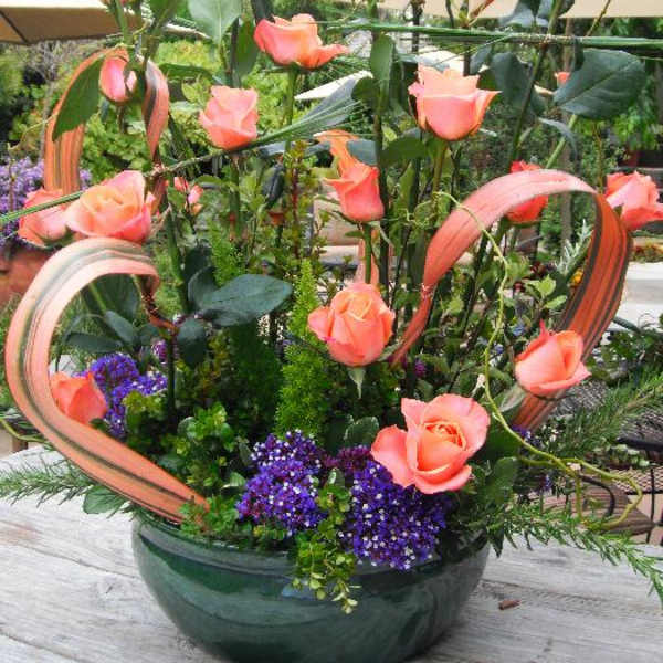 Tall arrangement of peach roses in a green bowl with ribbon loops