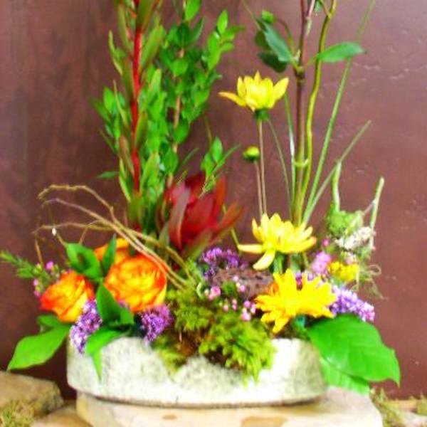 Tall mixed floral arrangement with yellow and orange blooms in a low container