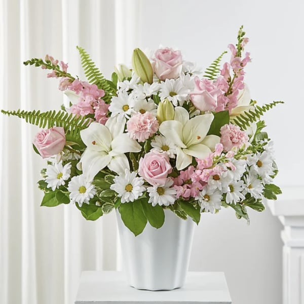 Pink roses and white lilies in a white vase with daisies and pink snapdragons