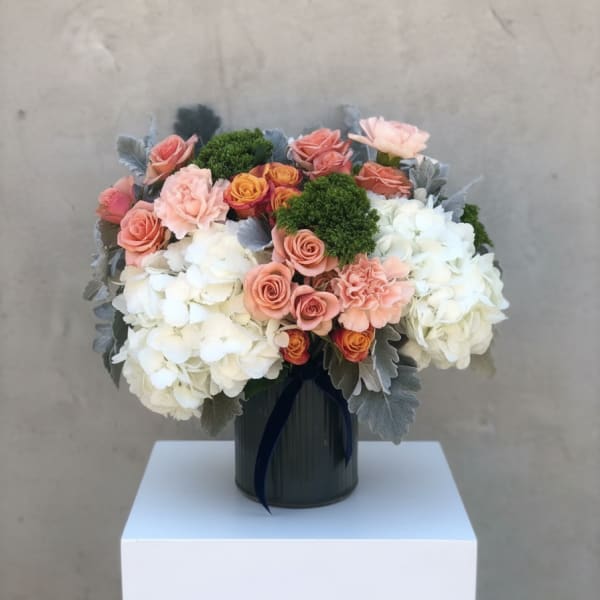 Low arrangement of white hydrangeas and peach roses in a dark ribbed vase with silver foliage