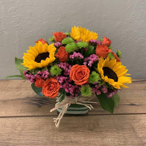 Bouquet of sunflowers, orange roses, and pink filler flowers in a striped vase