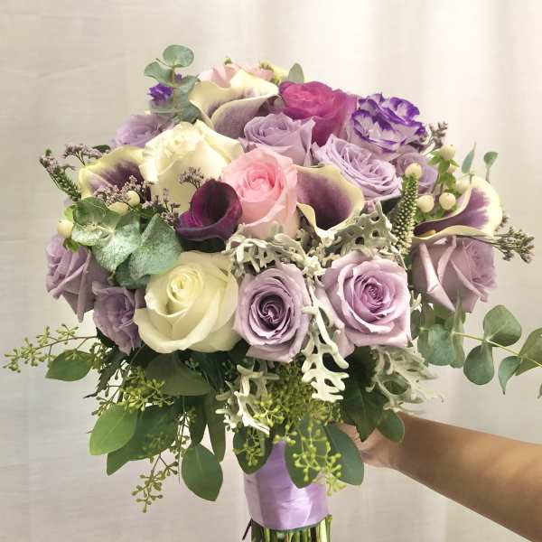 Handheld bouquet of pastel roses and calla lilies with greenery