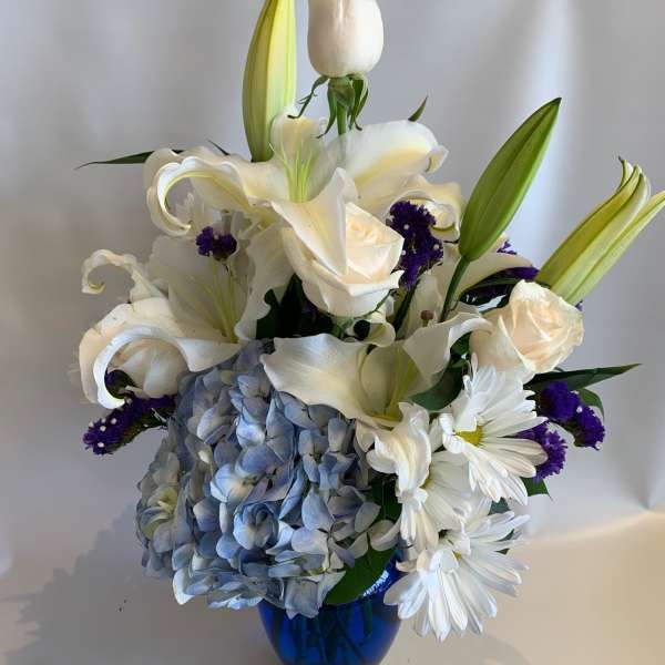 White lilies, roses, and blue hydrangea in a blue vase