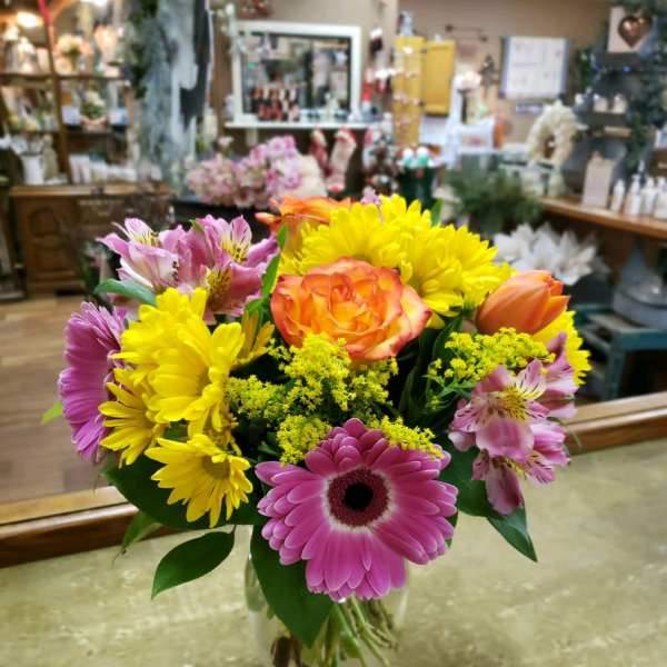 Mixed bouquet of pink, yellow, and orange flowers in a glass vase