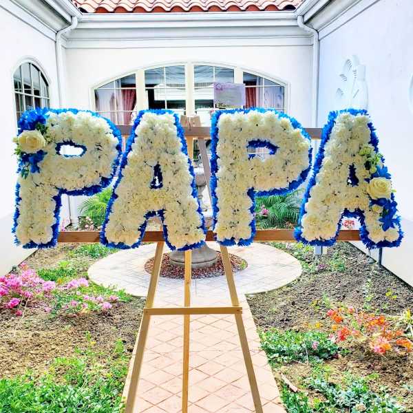 Floral letters spelling PAPA on an easel with white and blue flowers