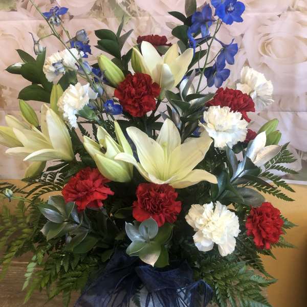 Arrangement of white lilies, red and white carnations, and blue delphinium in a vase
