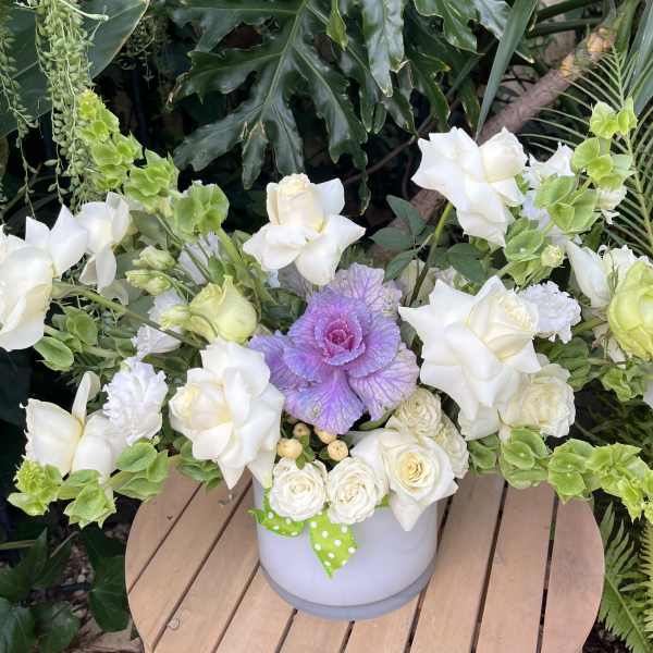 White roses and green snapdragons in a white vase with a purple cabbage center