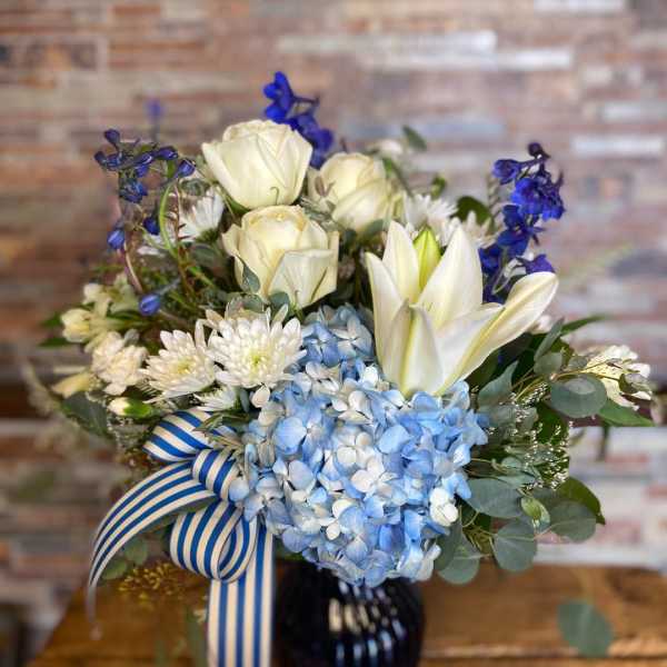 Blue and white bouquet with roses, hydrangeas, lilies, and a striped ribbon in a vase